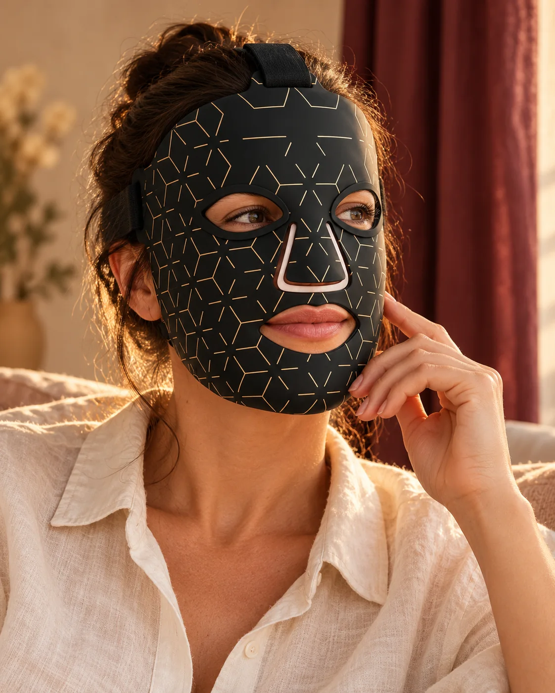Une femme porte le masque LED Éclavie noir et or dans un intérieur chaleureux.